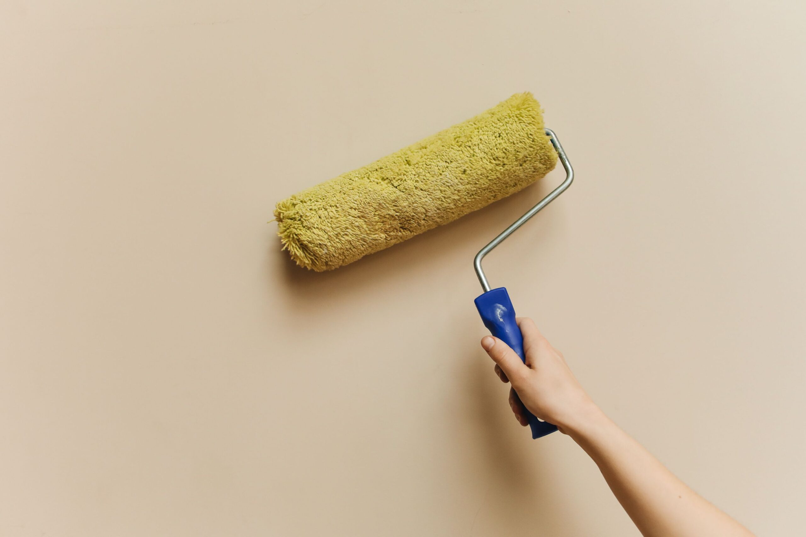Mano aplicando pintura con rodillo amarillo sobre pared color beige
